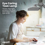 Eye-caring 26-inch silver LED desk lamp with clamp providing flicker-free lighting over a desk, helping reduce eye strain while working on a laptop.