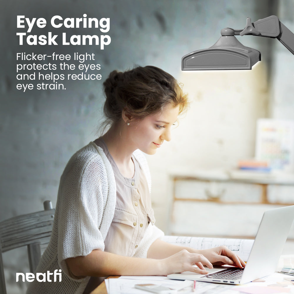 Eye-caring 26-inch silver LED desk lamp with clamp providing flicker-free lighting over a desk, helping reduce eye strain while working on a laptop.