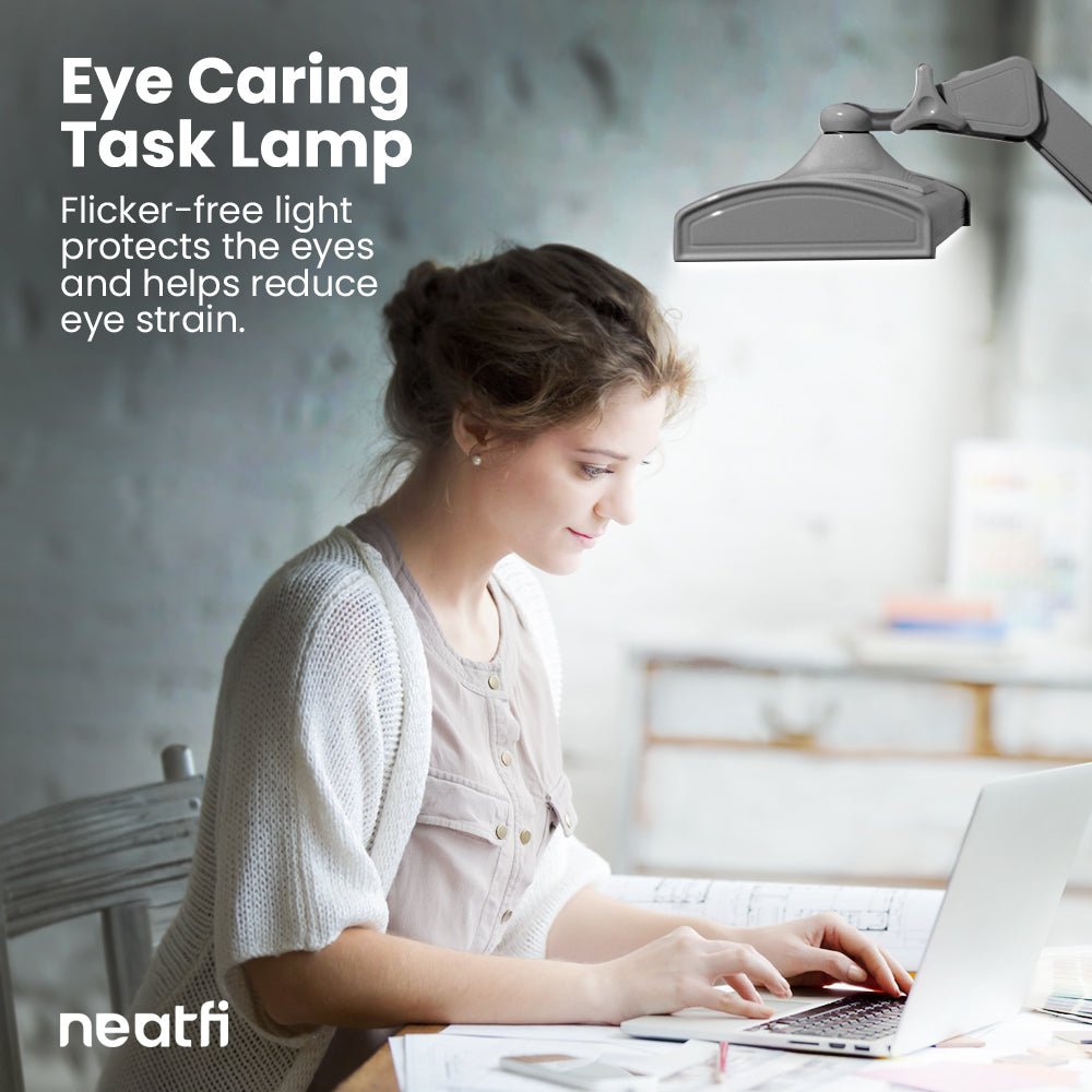 Eye-caring 26-inch silver LED desk lamp with clamp providing flicker-free lighting over a desk, helping reduce eye strain while working on a laptop.